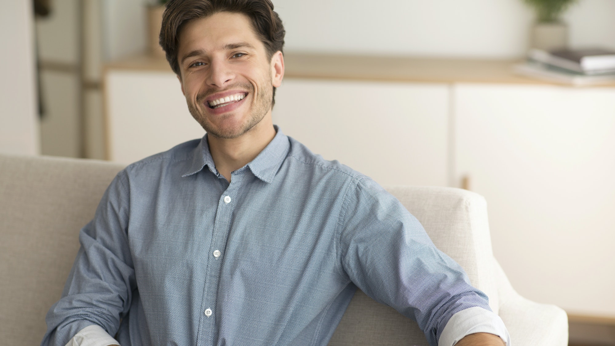 Cheerful Guy Smiling At Camera Resting On Couch At Home