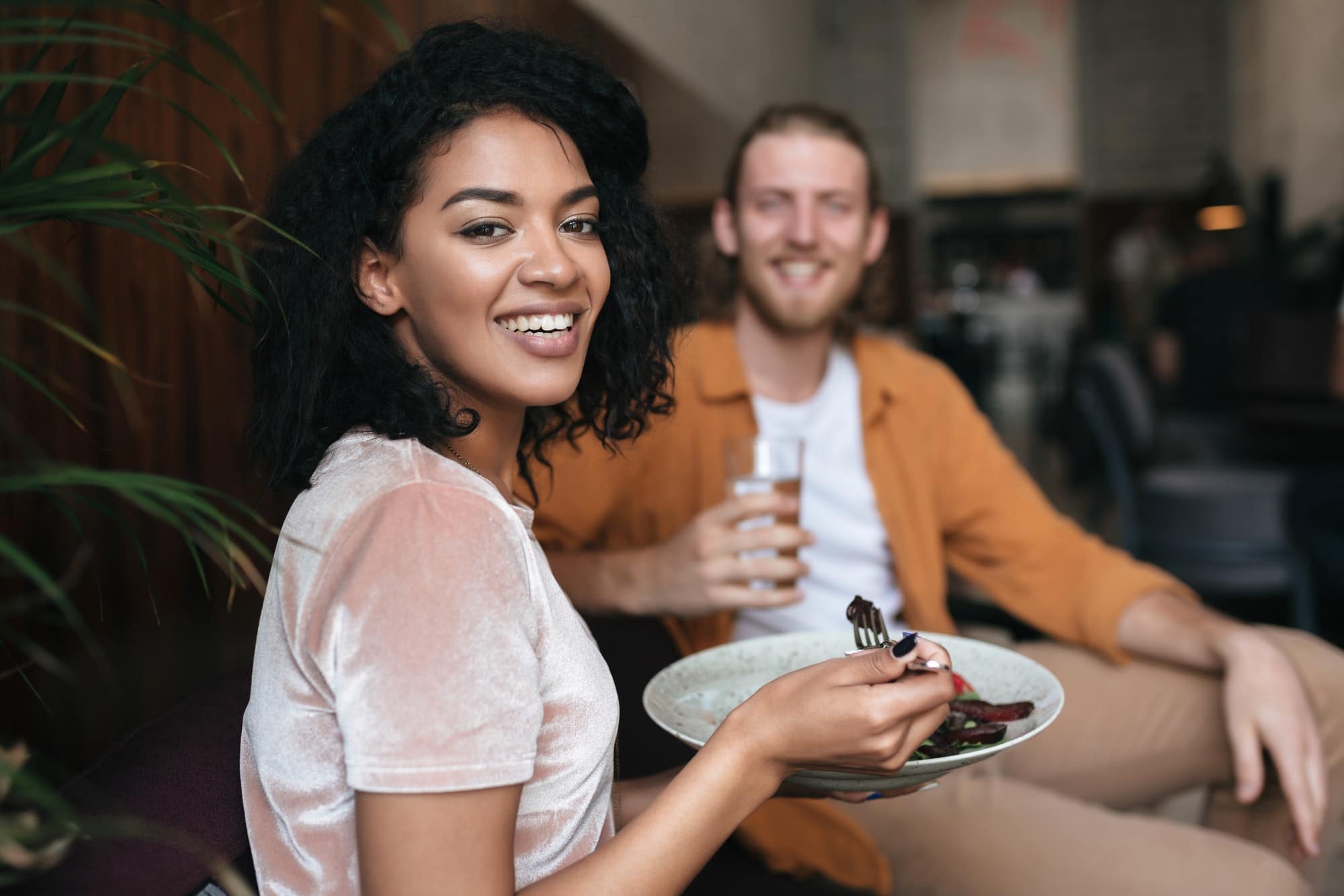 Nice African American lady sitting at cafe with plate of salad in hand
